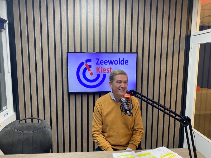 wethouder Erik van de Beld zit in een gele trui achter een microfoon in een radio studio