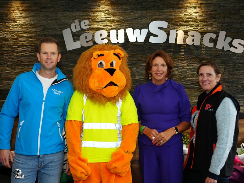 Drie mensen poseren naast een oranje leeuw.