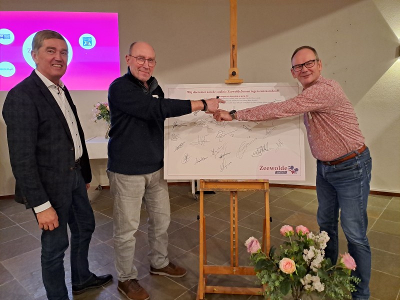 Twee mensen zetten hun handtekening op een groot vel papier.