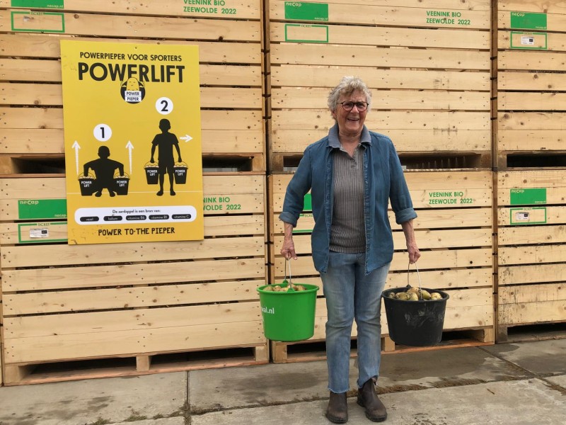 Truus enkele jaren terug voor een wand van kuubkisten met piepers, met 2 emmers Piepers in de emmer om te powerliften