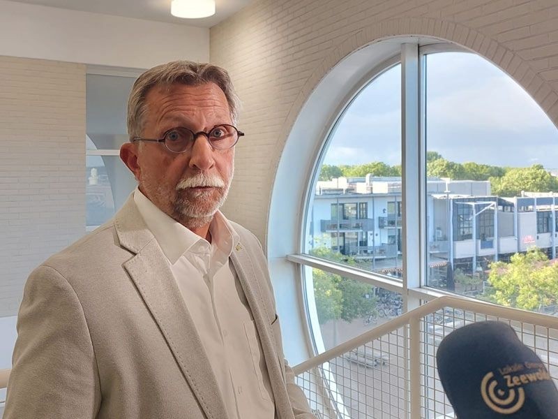 Wethouder met microfoon voor zich.