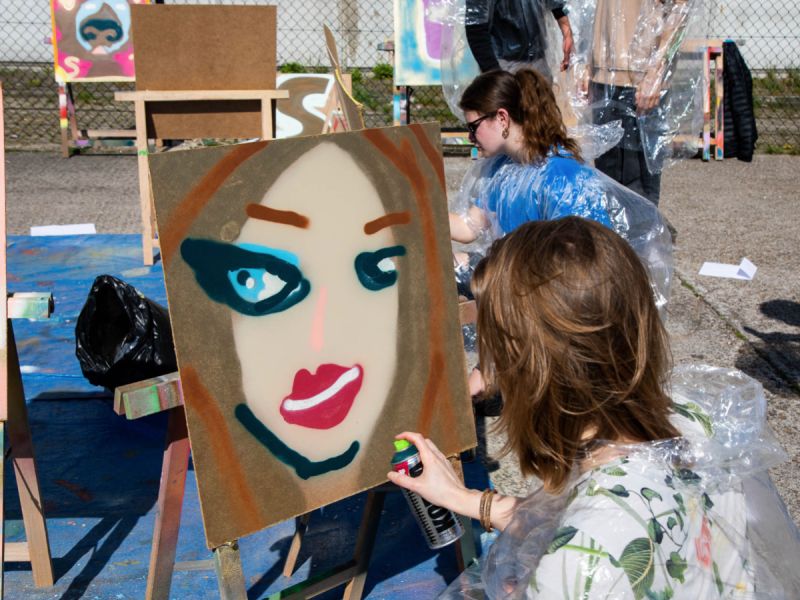 Graffiti workshop waar kinderen buiten op een houten plank graffiti spuiten