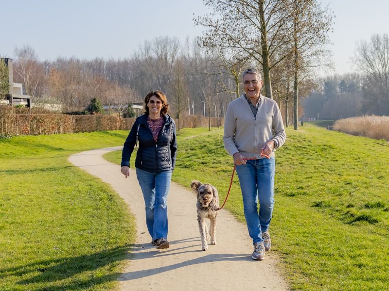 Een hond die aangelijnd wordt uitgelaten door een man en een vrouw die vrolijk lachen