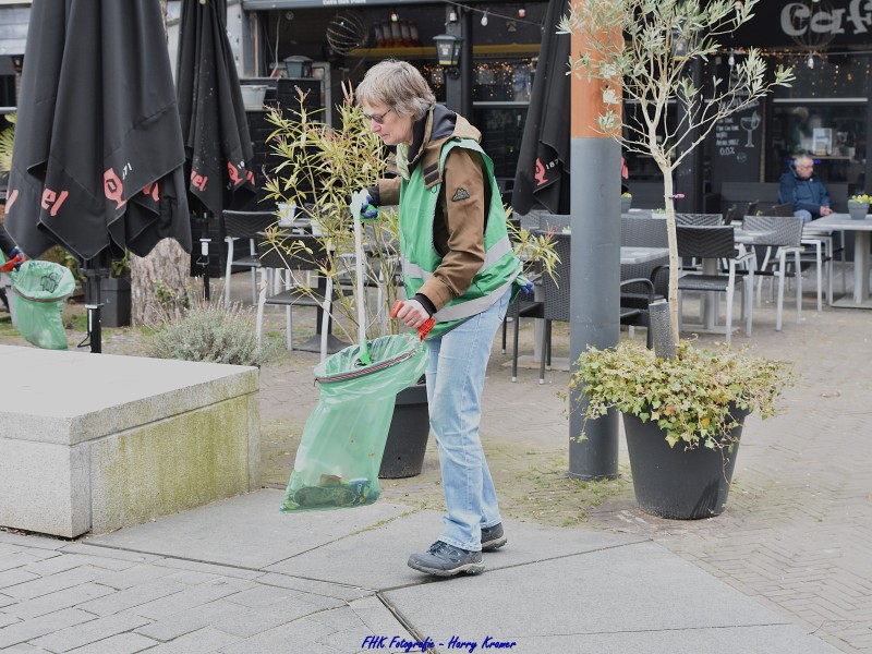 Een dame met afvalbrigade hesjes, grijper en zak met afval op het Kerkplein in Zeewolde