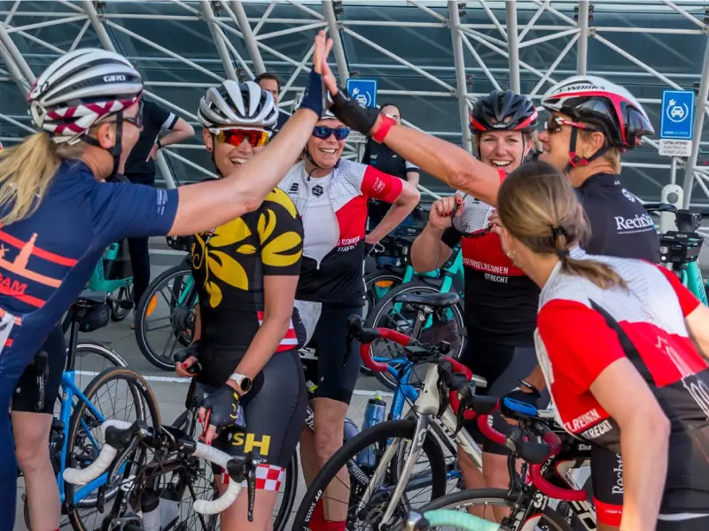 Een groep vrouwelijke wielrensters die juichend een high five doen