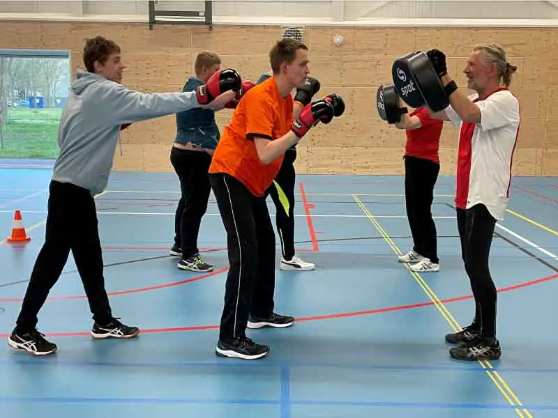 Een groep sporters met bokshandschoenen die tegenover de instructeur staat om te boksen.