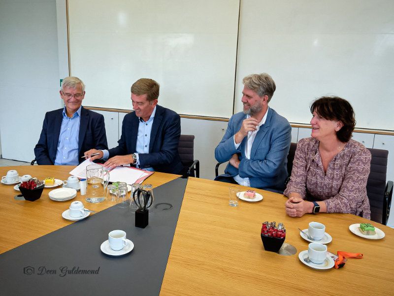 voer personen aan een vergadertafel , wethouder Erik van de Beld ondertekend het document, op tafel staan verder wat kopjes koffie 