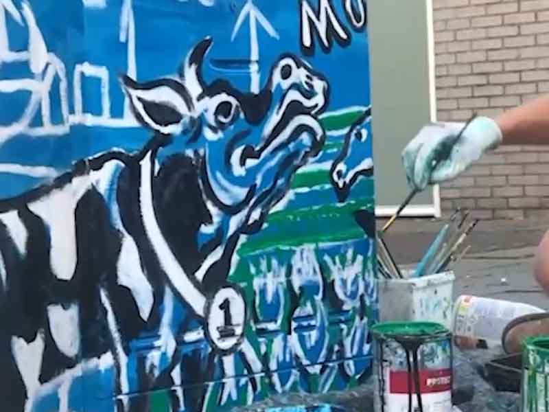 Een kastje waar aan geschilderd wordt, er wordt een koe van PInkendag geschilderd