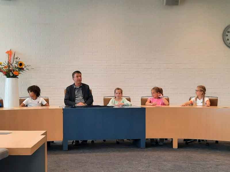 Wethouder bron en 4 kinderen op de zetels in de raadszaal
