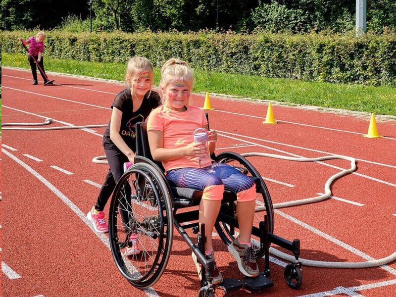 2 kinderen op de atletiekbaan met een rolstoel die samen spelletje spelen