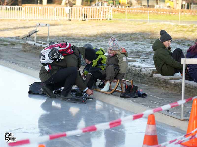 Een vader die de schaatsen omdoet bij zijn kinderen aan de rand van de ijsbaan