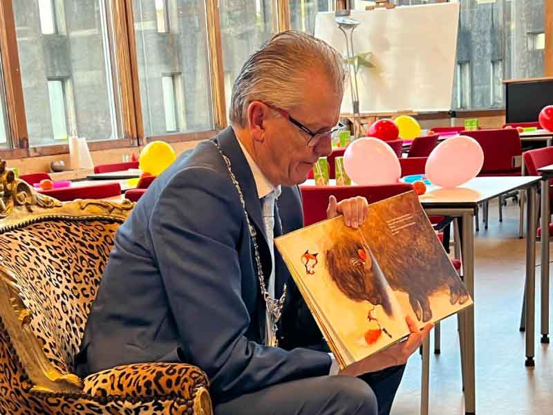 Burgemeester Gorter in fauteuil met panterprint en het prentenboek die hij laat zien aan kinderen