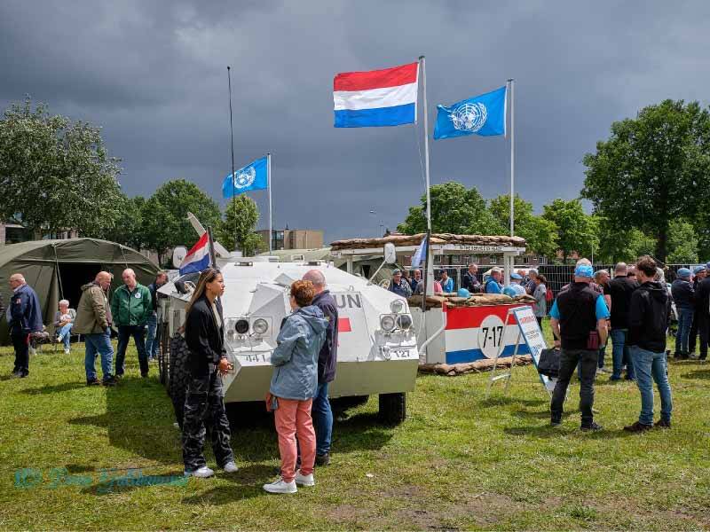 Op het evenemententerrein wat stands en defensievoertuigen waar mensen van de reunie omheen lopen. Ook 2 VN vlaggen en de Nederlandse vlag