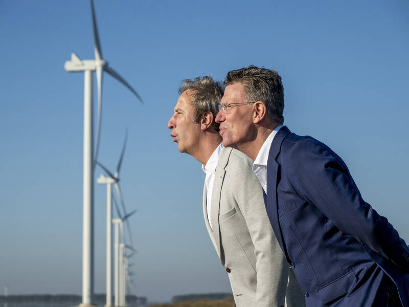 2 mannen die blazen naar de 2 windmolens in de verte 