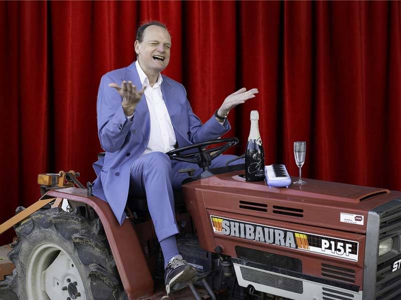 Vincent Bijlo op een klassieke tractor voor een theatergordijn