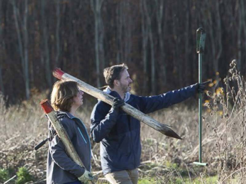 Een dame en heer wandelend door het voedselbos met palen op hun nek om te plaatsen met de gatenboor