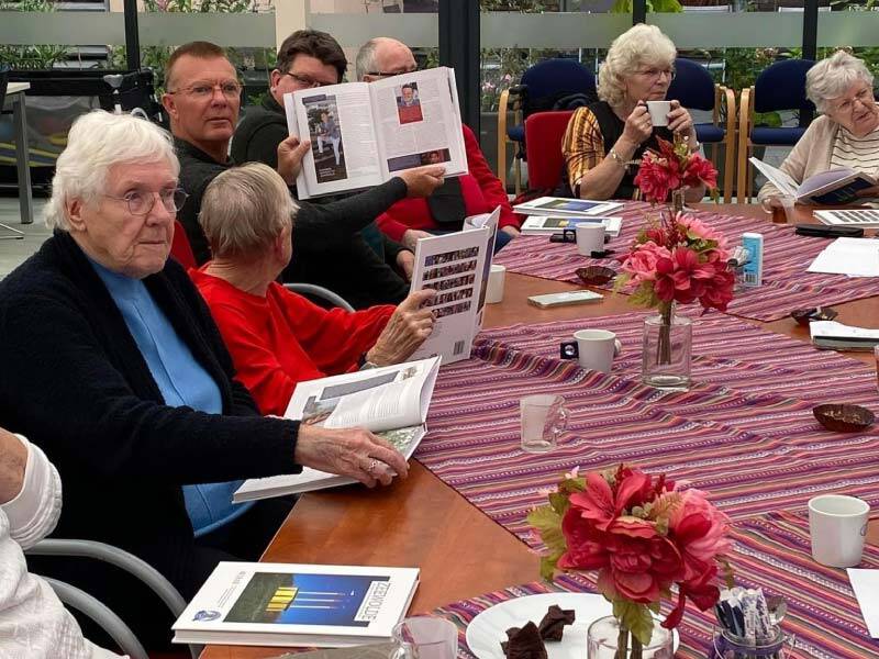 een aantal inwoners aan tafel met koffie, gebak en de boeken die ze samen bekijken