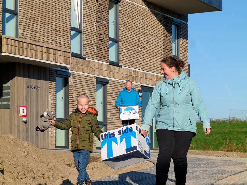 3 mensen die langs een huis lopen met dozen in hun hand