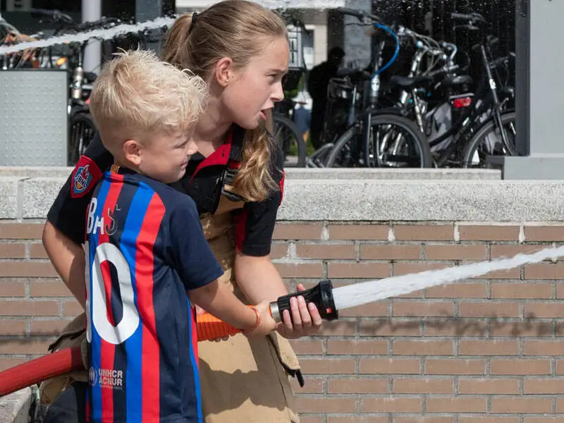 kindje met meisje van de jeugdbrandweer die water spuiten