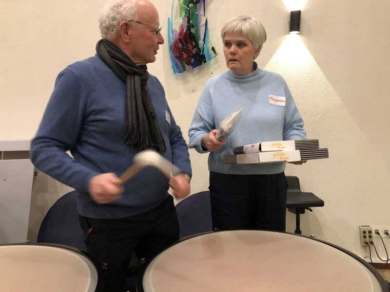 2 mensen bij trommels, 1 met stokken in de hand, de ander met een boekje