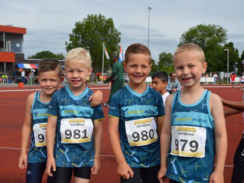 Vier jongens in blauwe sportkleding op een rode atletiekbaan .