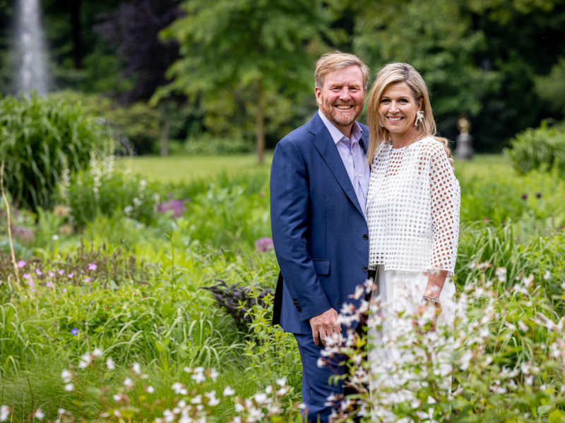Het Koninklijk Paar staat naast elkaar in een groene tuin met bloemen.