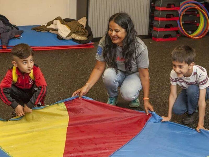Begeleider met kinderen die bij een gekleurd kleed staan