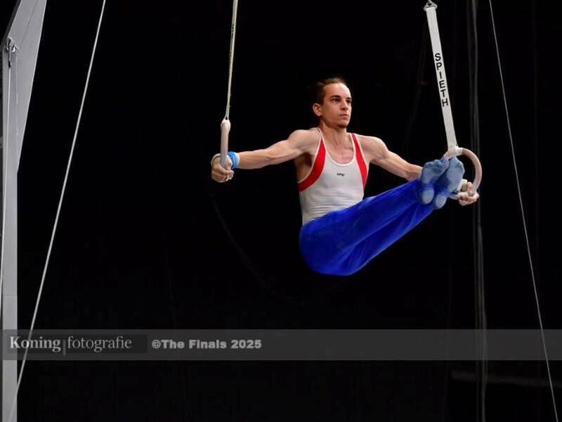 Turner op de ringen met blauwe sportbroek en wit met rood shirt.