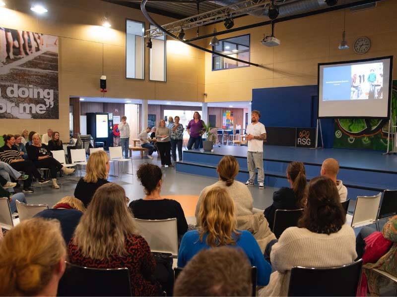 Lars Oostland voor een scherm in de zaal met ouders als publiek