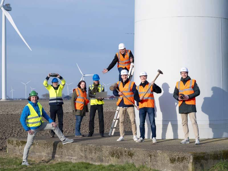 Saneerteam van Echt en Windpark bij een windmolen op het land, allen met een hesje en gereedschap in hand
