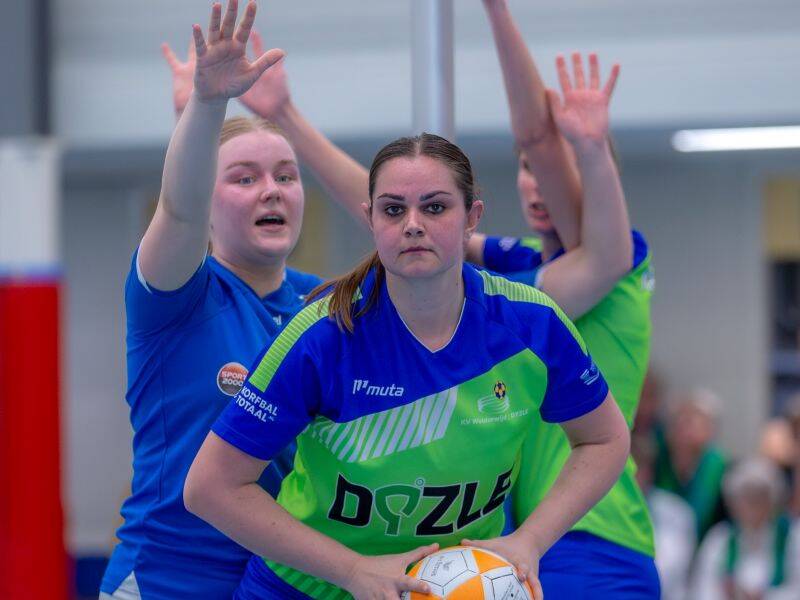 drie korfbalspelers twee op de achtergrond met handen omhoog een op de voorgrond met korfbal in handen