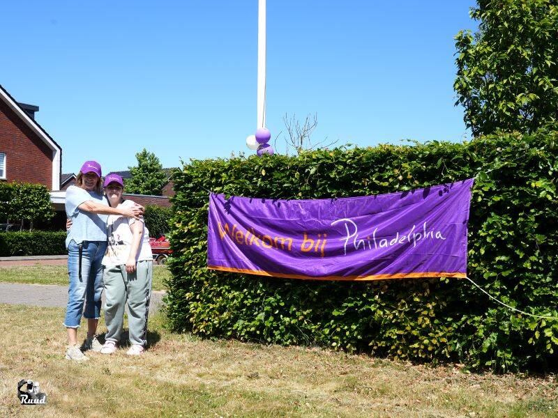 Twee mensen staan voor een paarse banner met tekst op een grasveld