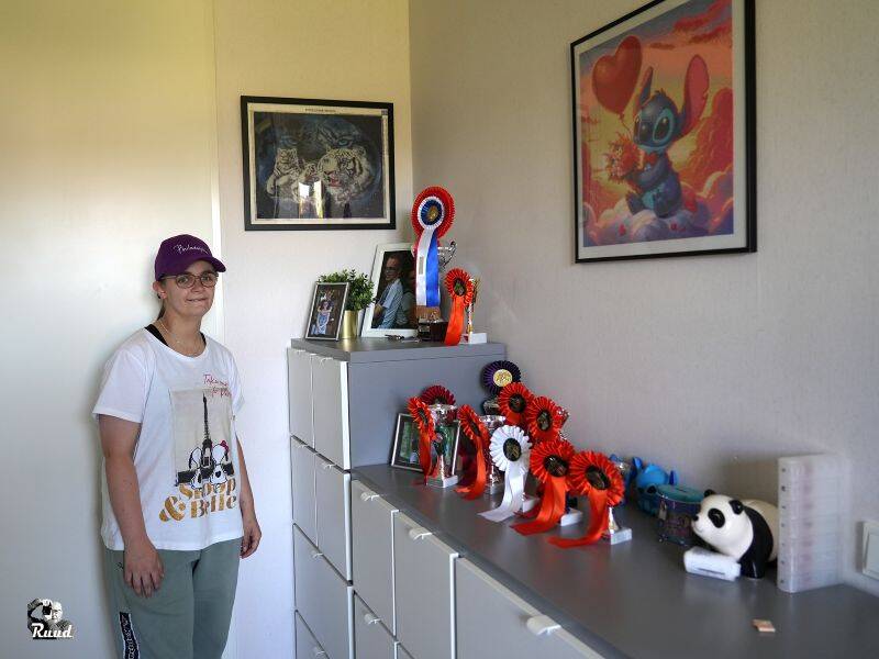 Persoon met paarse pet staat naast een kast met diverse prijzen erop