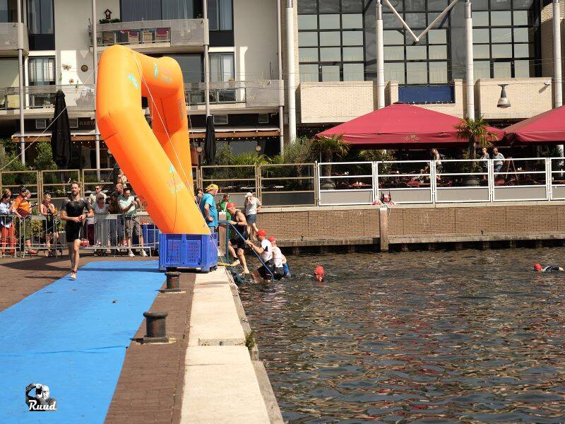 Zwemmers die in de aanloophaven uit het water komen en over de blauwe loper rennen om naar hun fiets te gaan